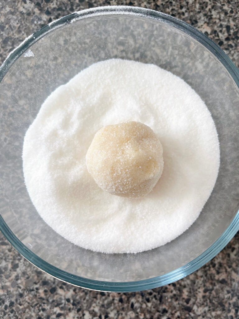 A ball of sugar cookie dough in a bowl of sugar.