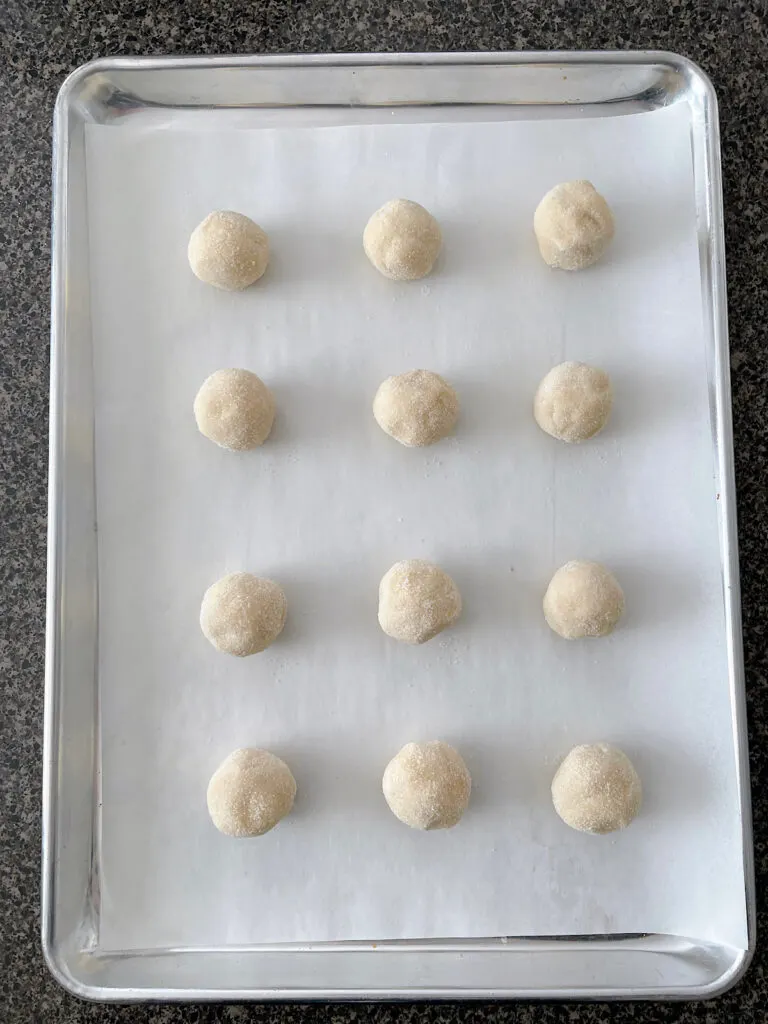 Sugar cookie dough balls on a parchment paper-lined baking sheet.