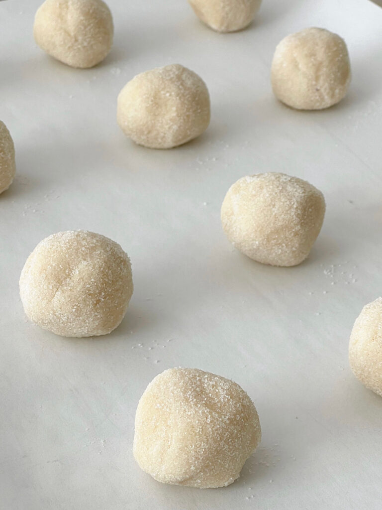 Sugar cookie dough balls on a parchment paper-lined baking sheet.