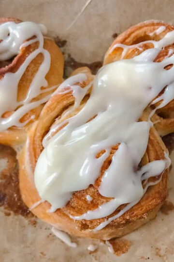A Mickey shaped cinnamon roll with cream cheese icing.