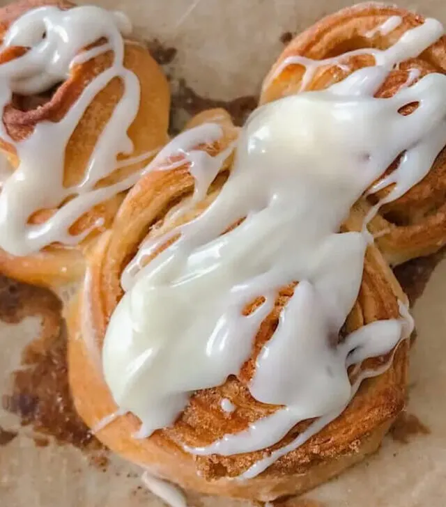 A Mickey shaped cinnamon roll with cream cheese icing.