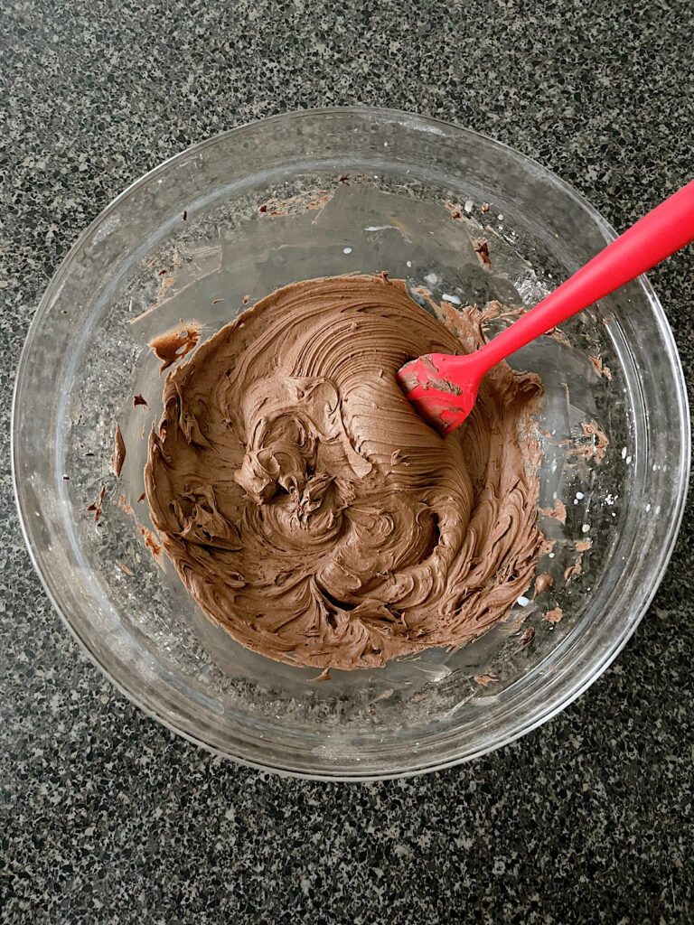 A bowl of chocolate buttercream with a red spatula.