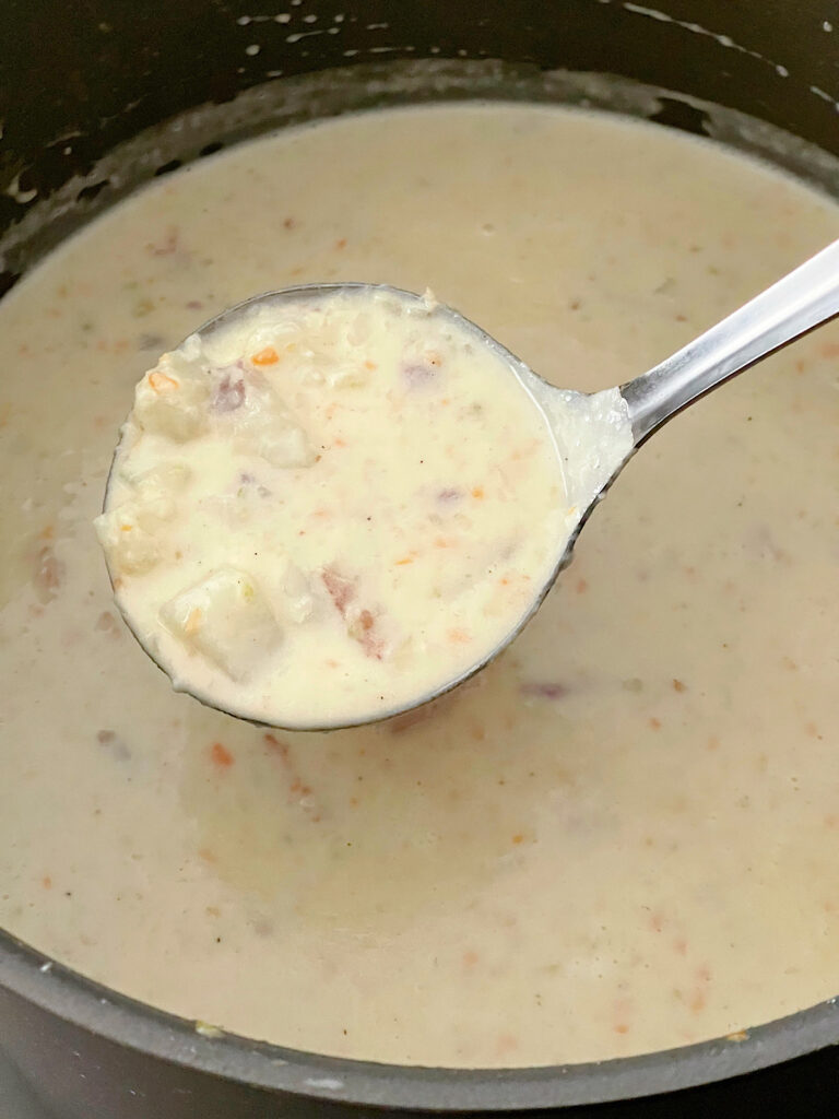 Loaded baked potato soup in a ladle over a pot of soup.