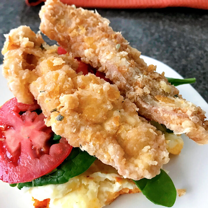 Two pieces of sage fried chicken on a white plate with tomatoes and spinach.