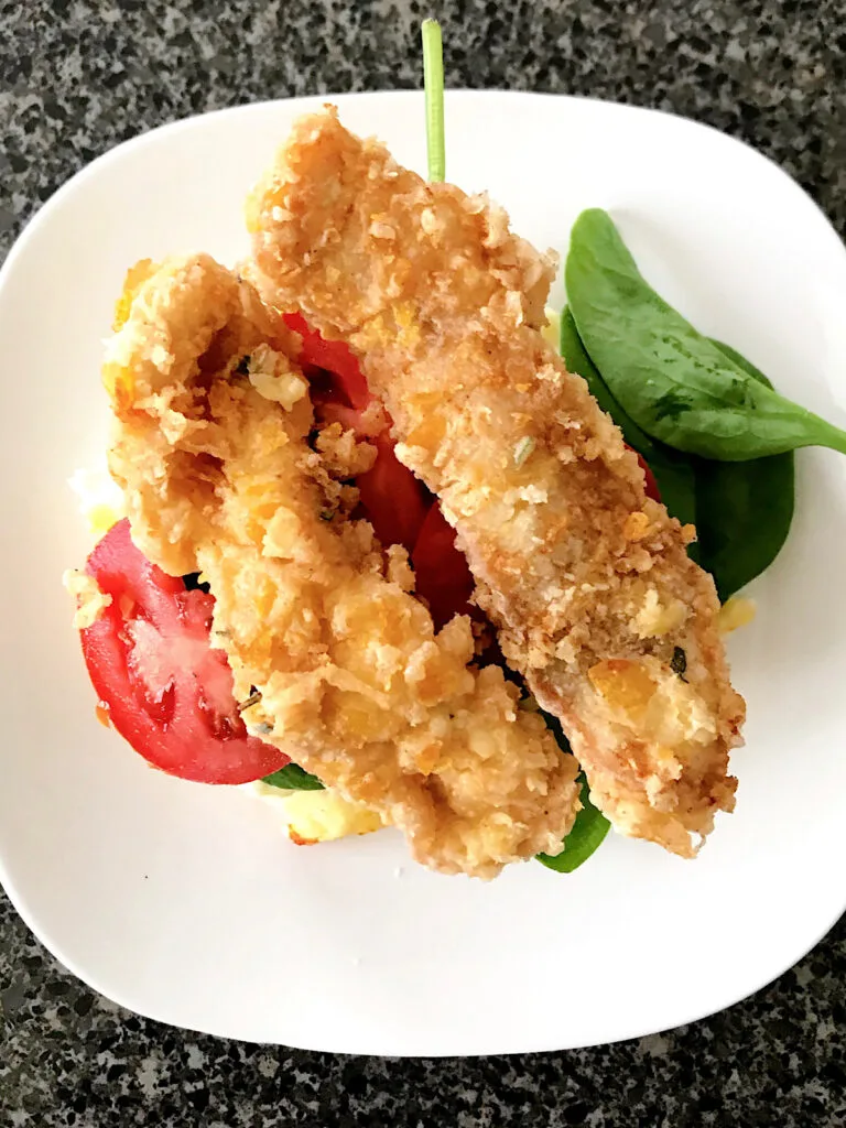 Two pieces of sage fried chicken on a white plate with tomatoes and spinach.