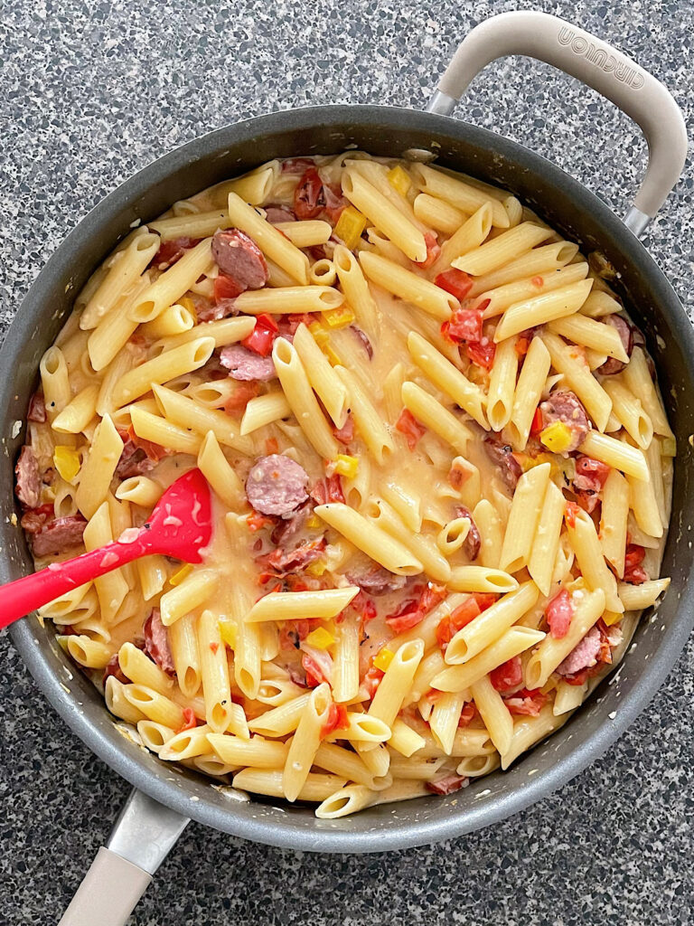 Penne pasta, sausage, and peppers in a sauce pan.