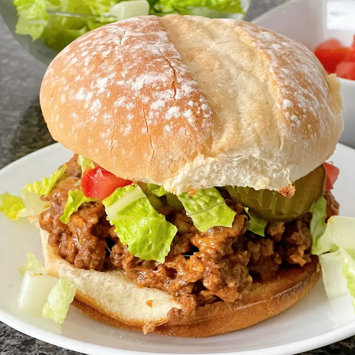 A cheeseburger sloppy joe topped with shredded lettuce, tomatoes, and pickles.