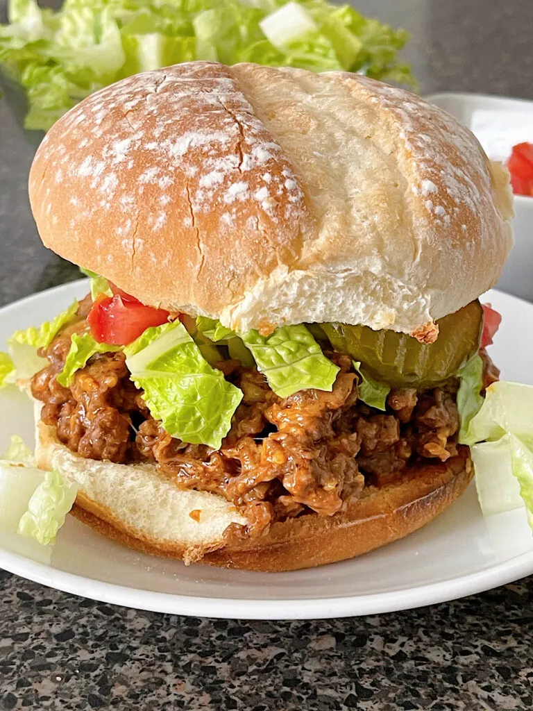 A cheeseburger sloppy joe topped with shredded lettuce, tomatoes, and pickles.