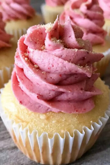 A strawberry cheesecake cupcake with strawberry buttercream and graham cracker crumbs.