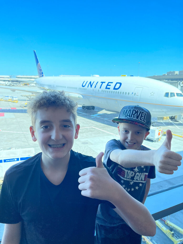 Two kids at the San Francisco Airport in front of a United Airlines airplane.