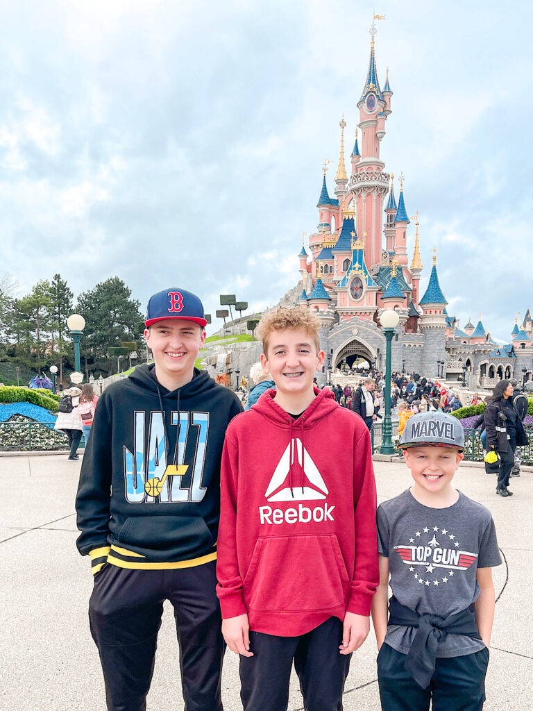 Three kids standing in front of Sleeping Beauty Castle at Disneyland Paris.