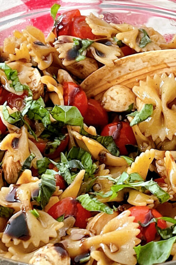Caprese Pasta Salad in a glass bowl with a wooden spoon.