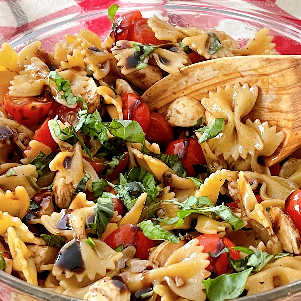 Caprese Pasta Salad in a glass bowl with a wooden spoon.