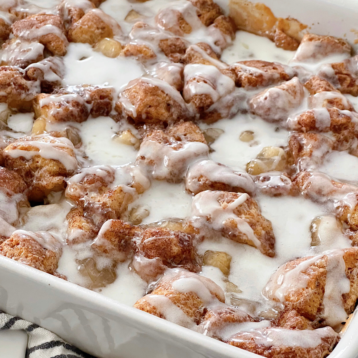 An apple cinnamon roll bake with icing in a baking dish.