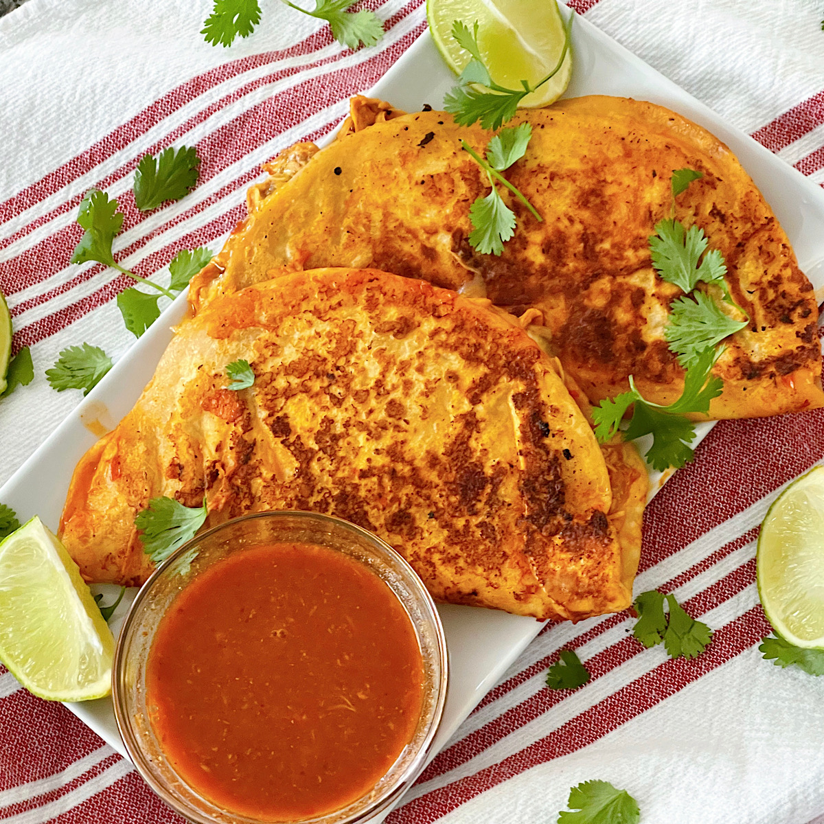 Two chicken birria tacos on a plate with a bowl of consumme.