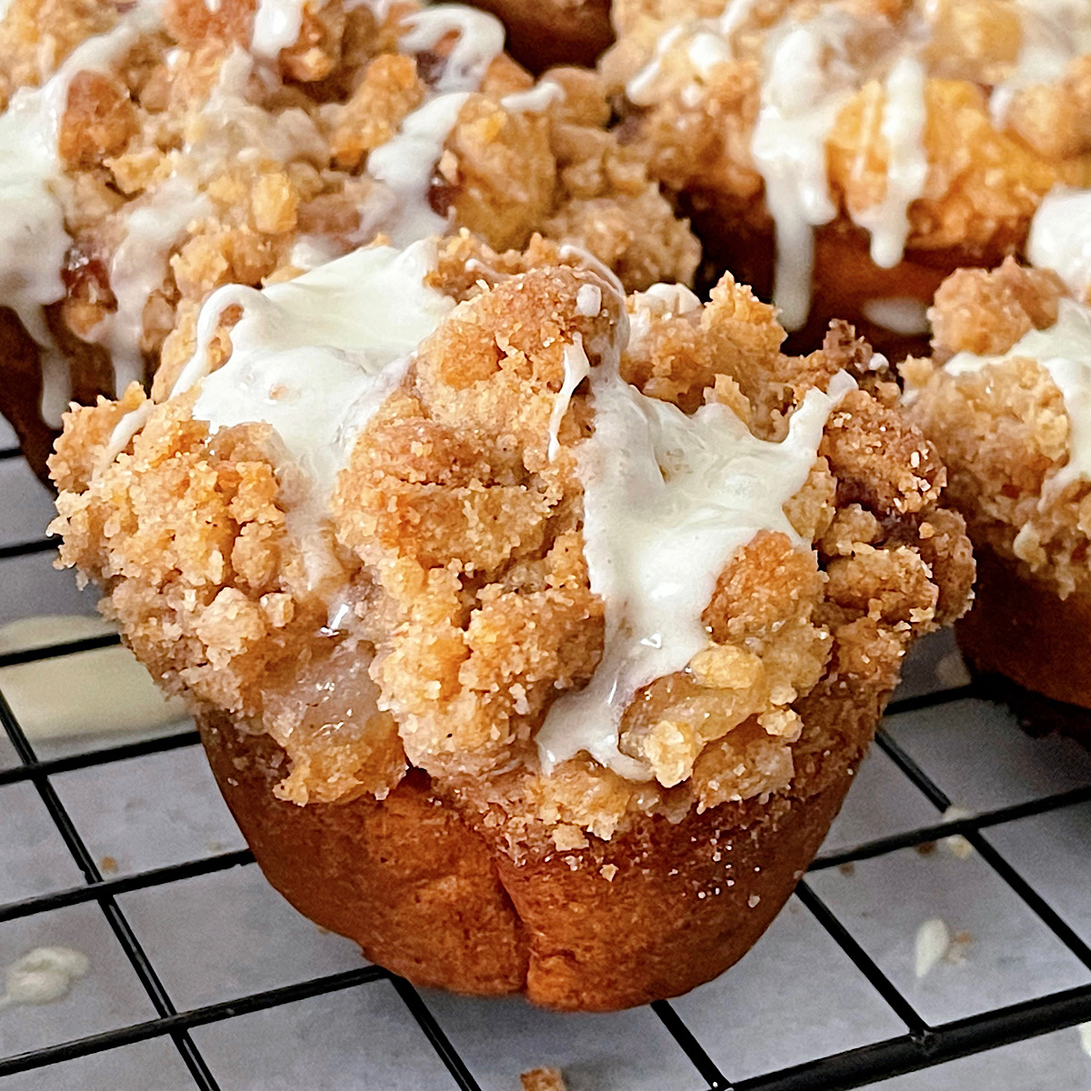 A cinnamon roll shaped like a muffin filled with apple pie filling, topped with streusel, and drizzled with icing.
