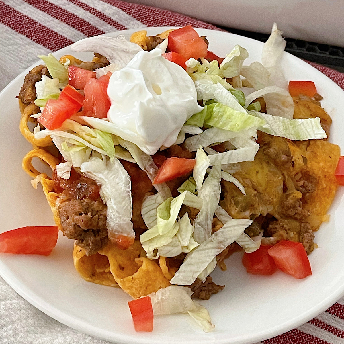 A serving of Walking Taco Casserole topped with lettuce, tomato, and sour cream.