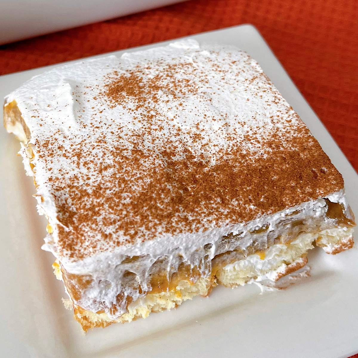 A slice of Twinkie Pumpkin Delight with layers of Twinkies, no bake cheesecake, pumpkin pie, and whipped cream.