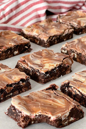 Brownies topped with melted peppermint bark candies with a red and white kitchen towel.