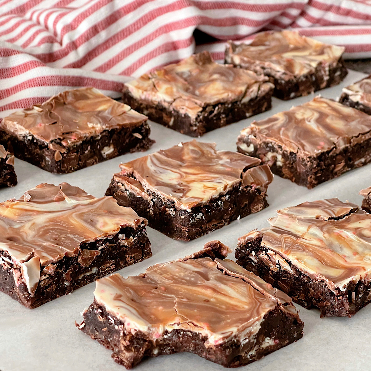 Brownies topped with melted peppermint bark candies with a red and white kitchen towel.