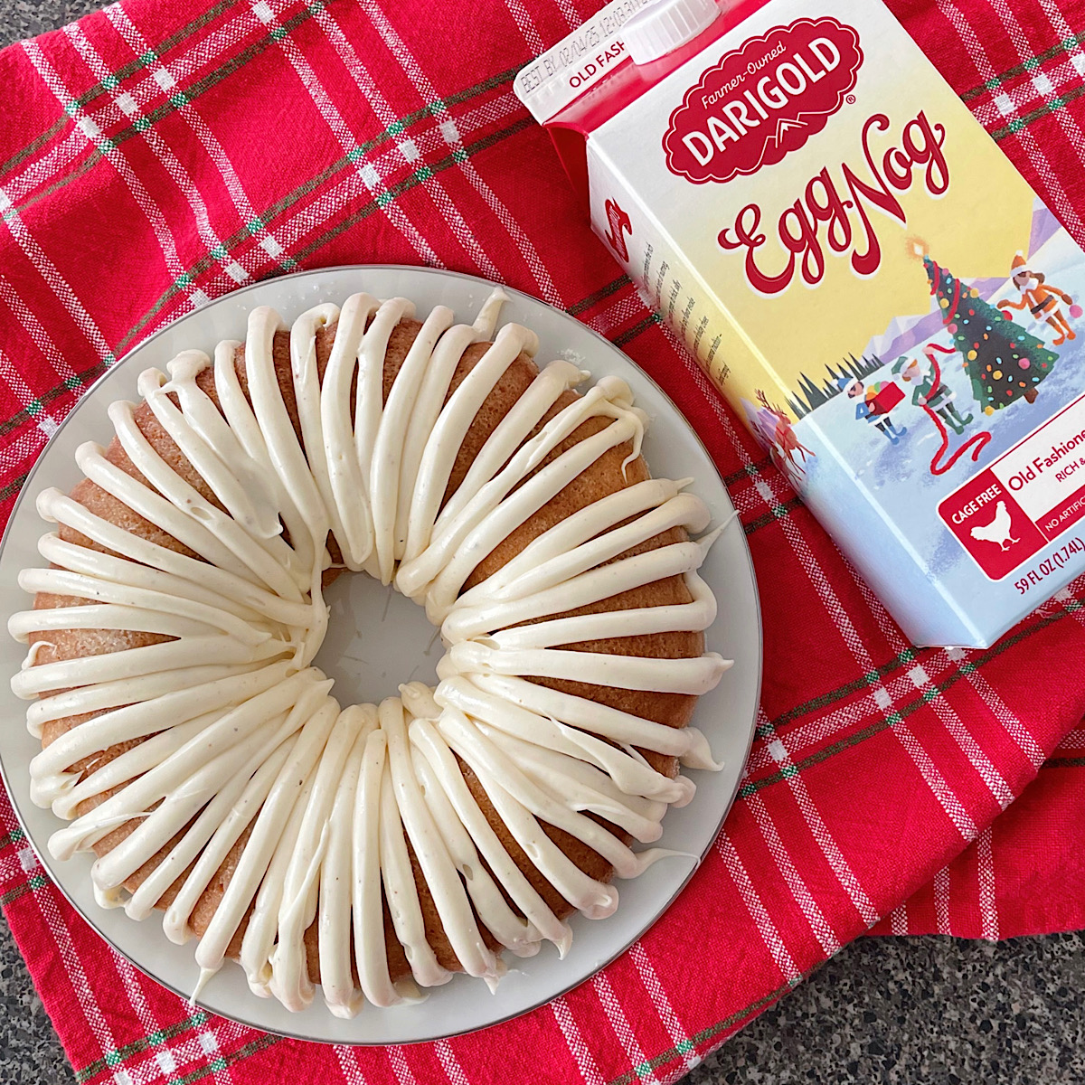 An eggnog bundt cake with eggnog frosting and a carton of eggnog.