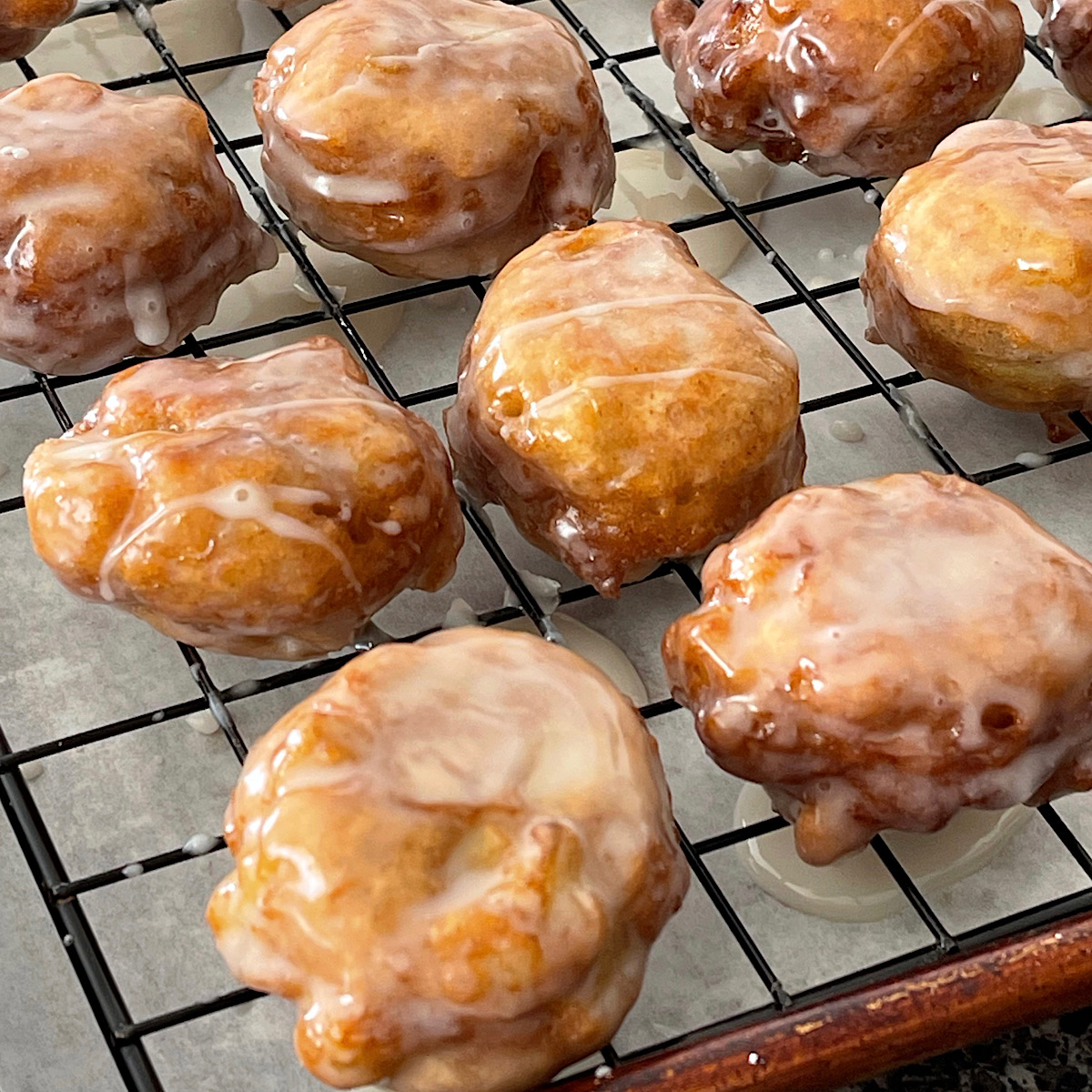 Mini apple fritters coated in glaze on a cooling rack.