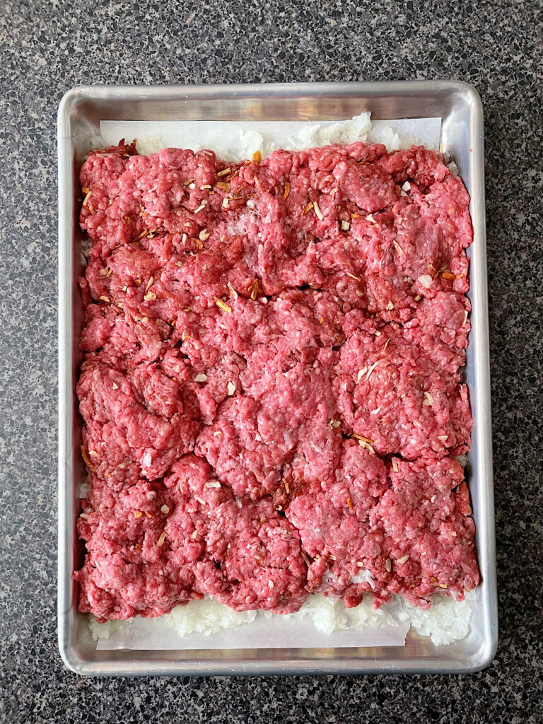 Ground beef made in to a large patty on a baking sheet.