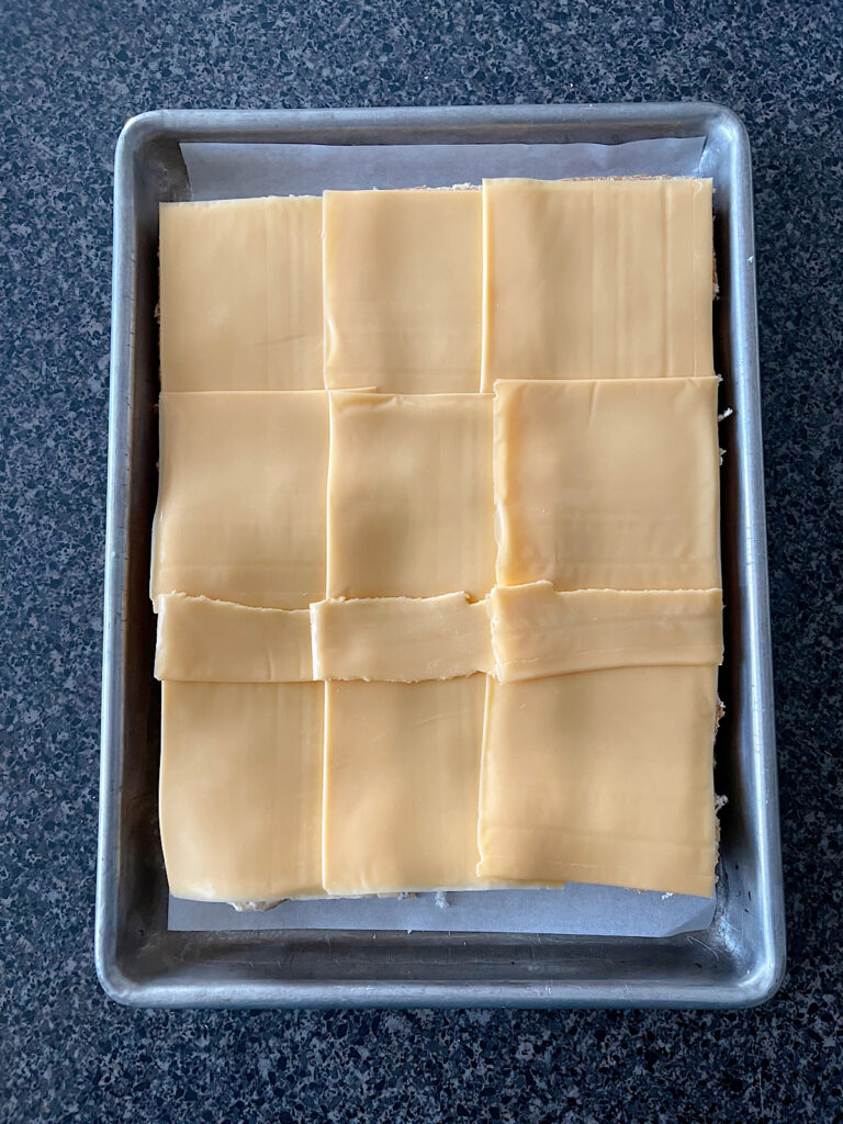 A layer of American cheese slices on dinner rolls that have been cut in half.