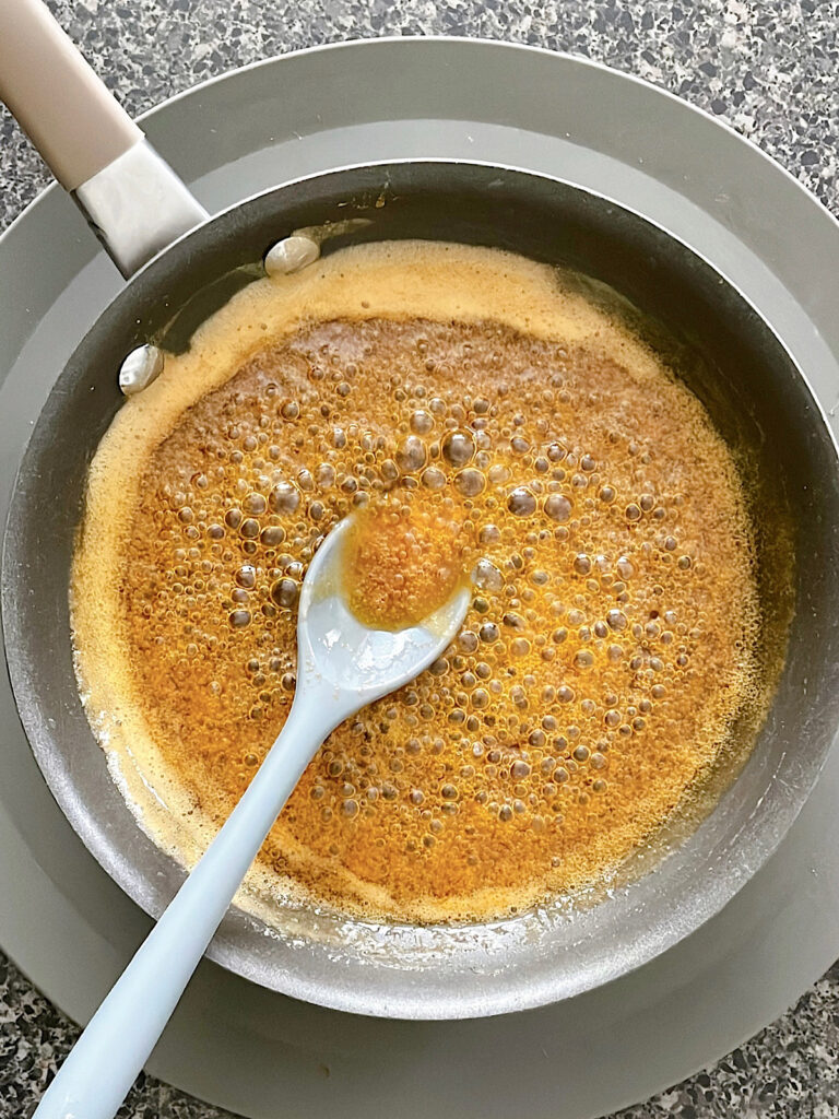 Hot honey sauce in a pan with a grey spoon.