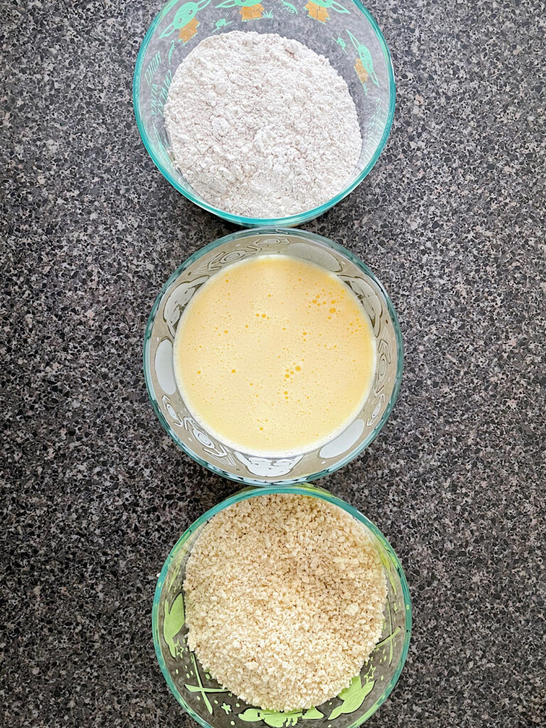 A set of three shallow bowls with flour, egg, and panko breadcrumbs.