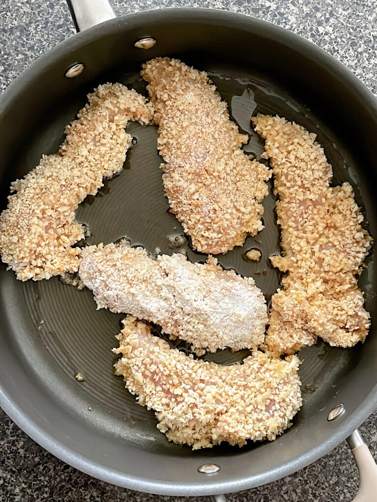 Chicken tenders cooking in a pan.