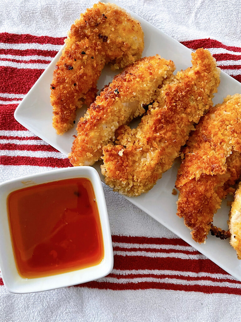 Chicken tenders on a white plate with a dish of hot honey.