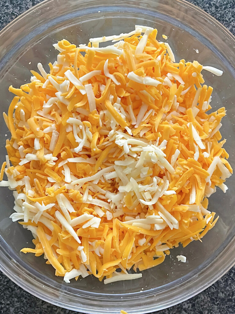 Sharp Cheddar and Gruyere cheese in a clear mixing bowl.