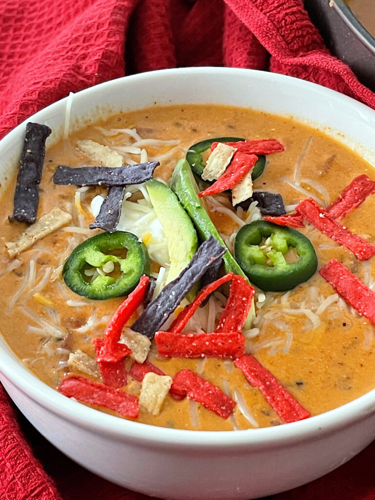 A bowl of cheesy enchilada chili topped with sour cream, jalapenos, and tortilla strips.