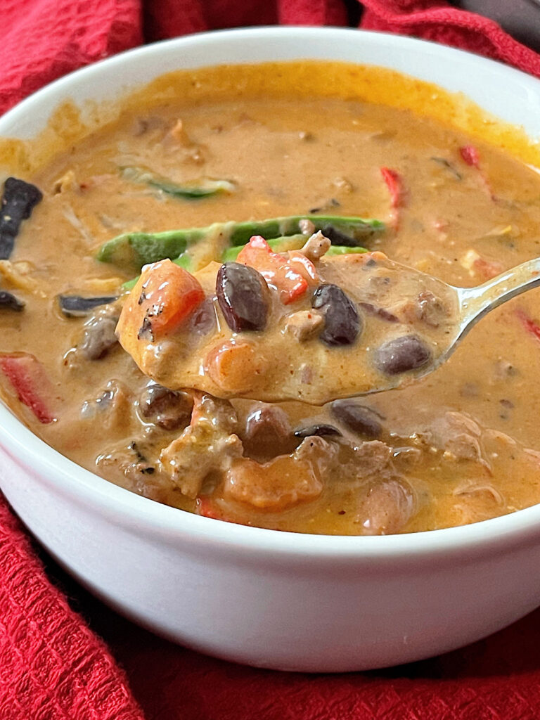 A bowl of cheesy enchilada chili topped with sour cream, jalapenos, and tortilla strips.