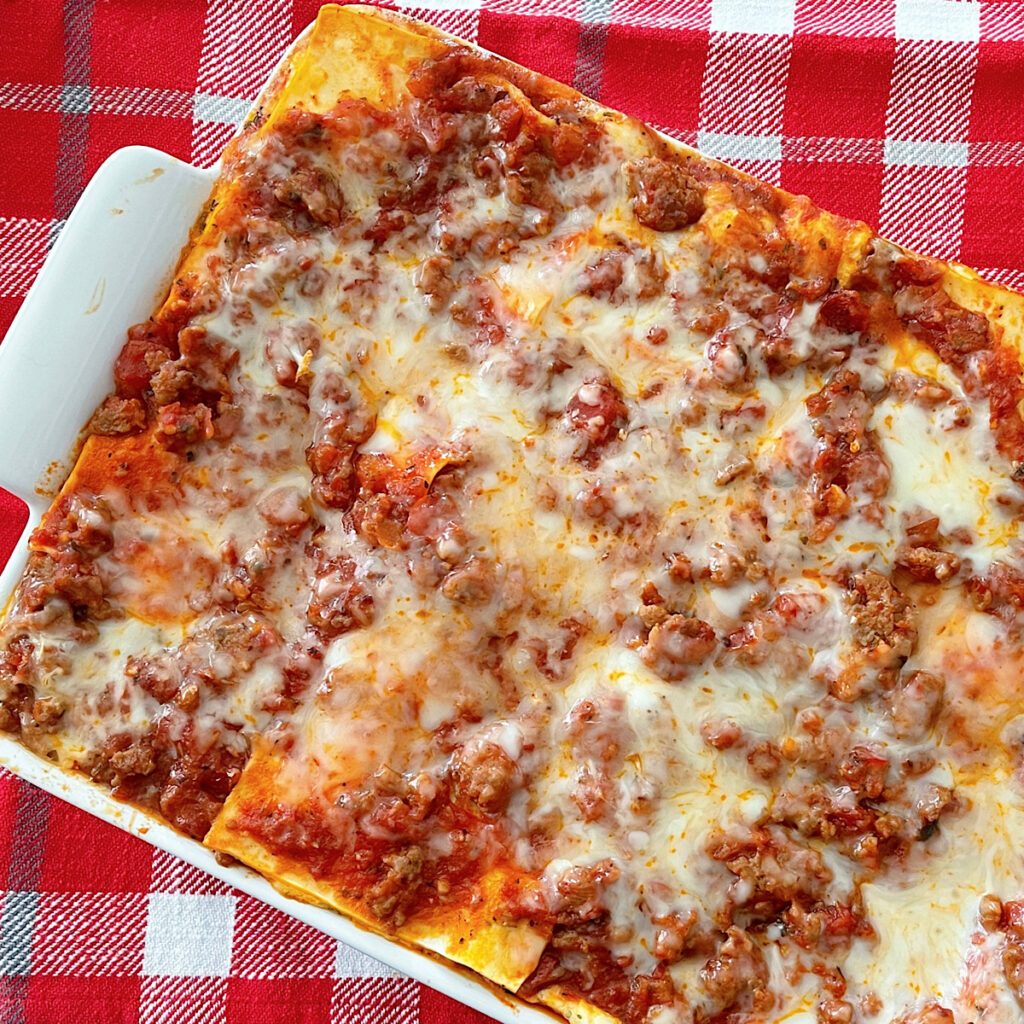 Million Dollar Lasagna in a white dish with a red plaid background.