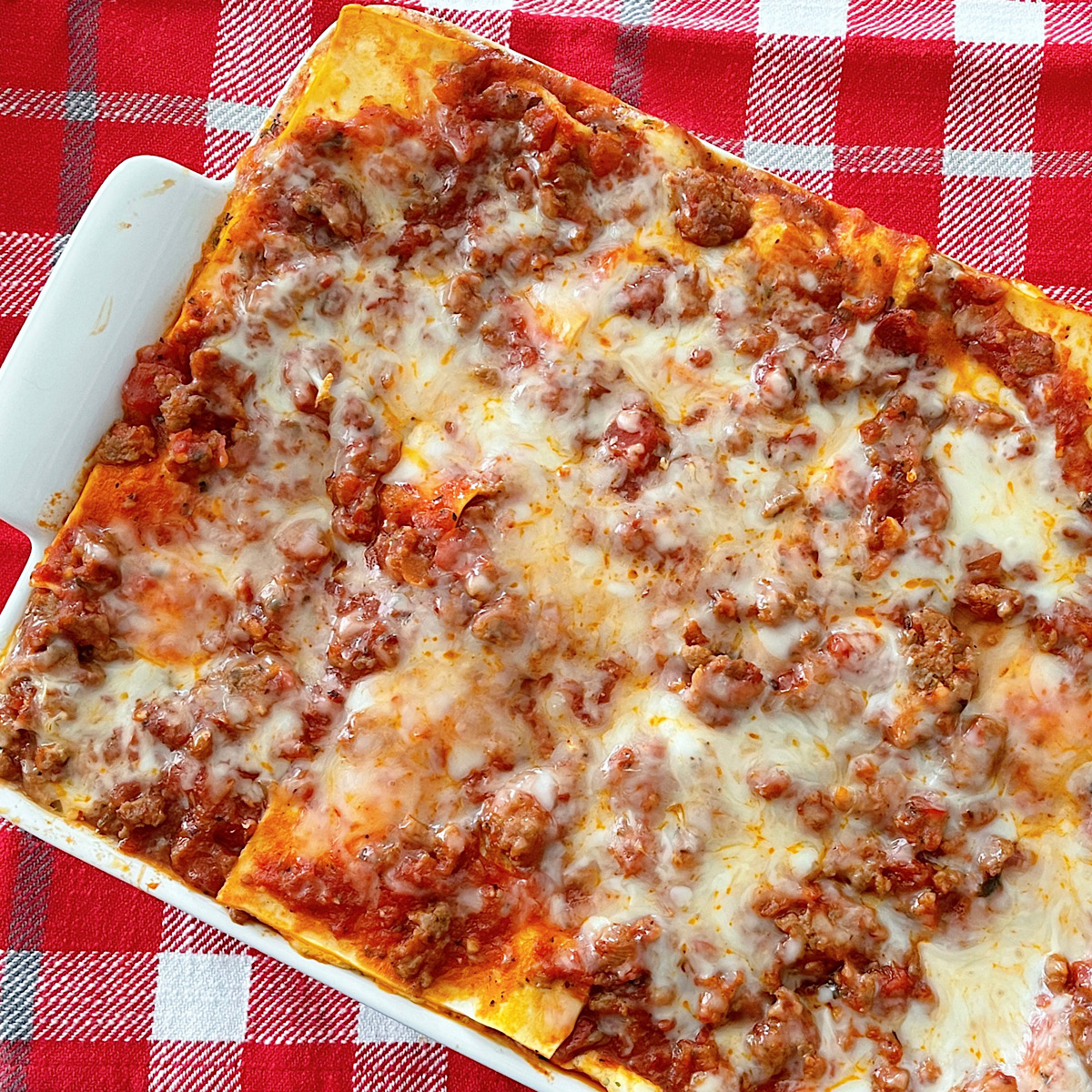 Million Dollar Lasagna in a white dish with a red plaid background.
