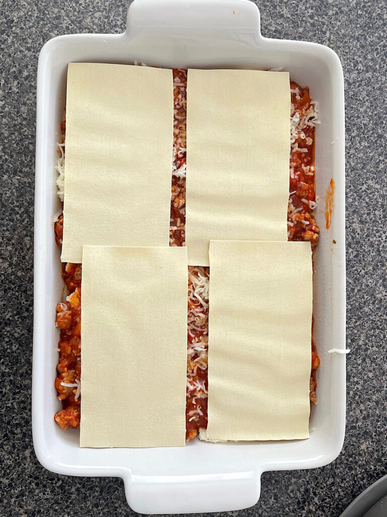 Lasagna being assembled in a white dish.
