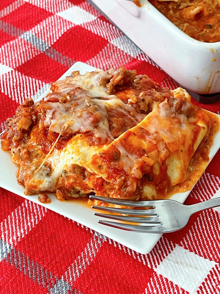 A slice of lasagna on a white plate with a fork.