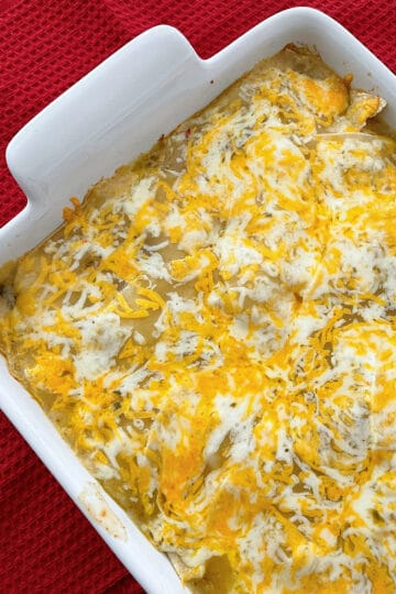 Baked green chicken chile enchiladas in a white baking dish.