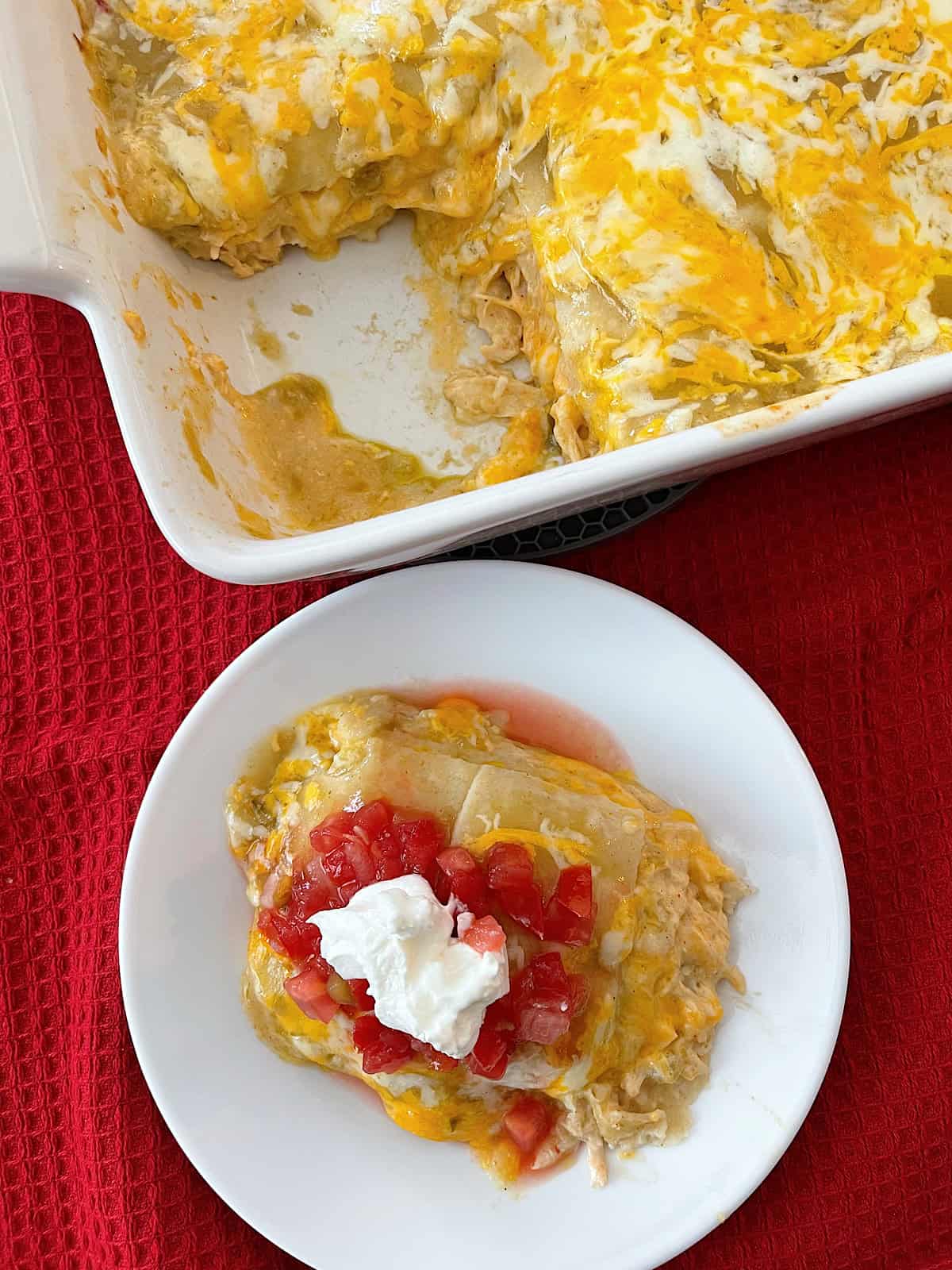 Stacked green chile chicken enchiladas on a plate and in a baking dish.