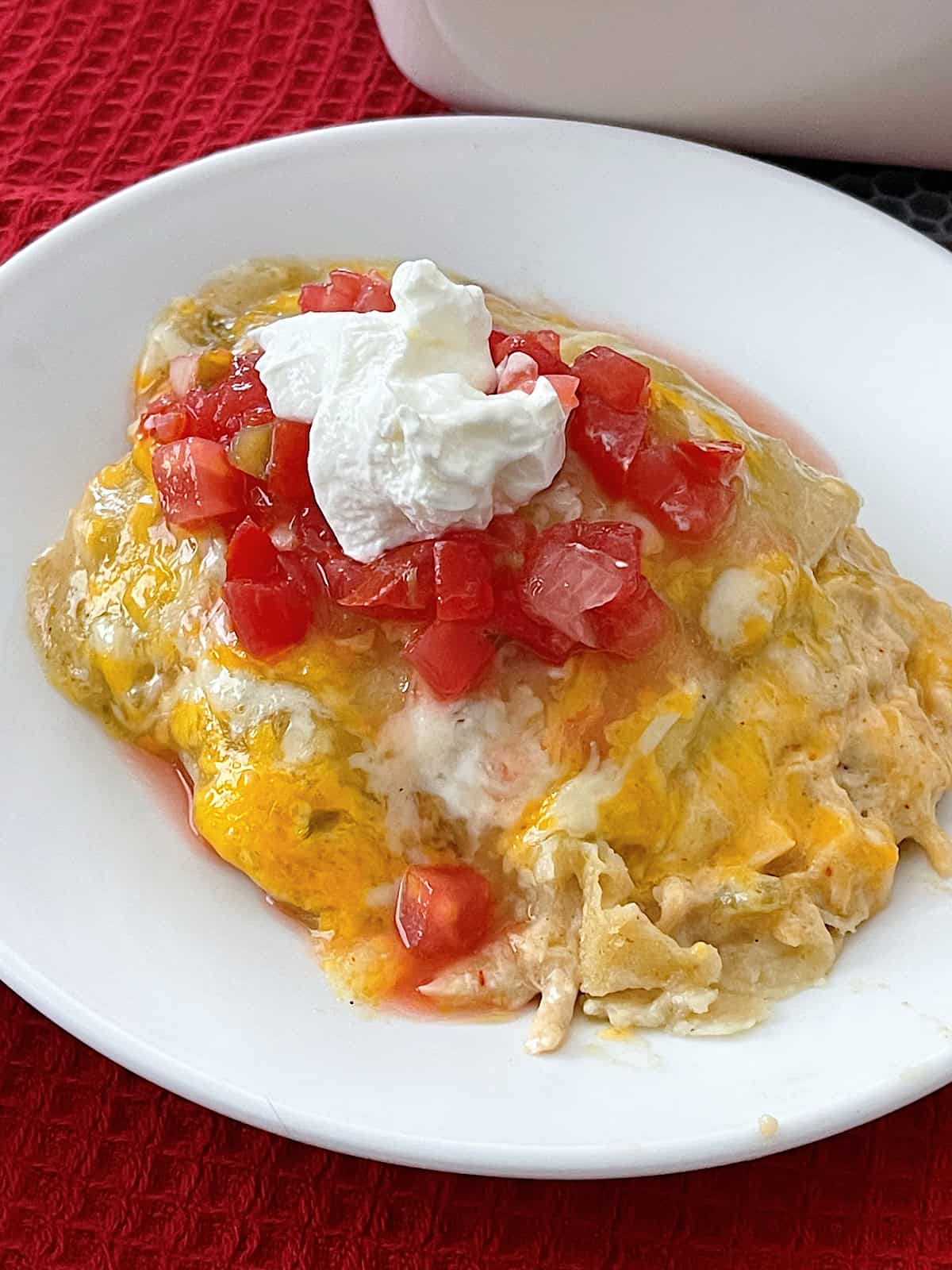 Green chile chicken enchiladas on a white plate with pico de gallo and sour cream.
