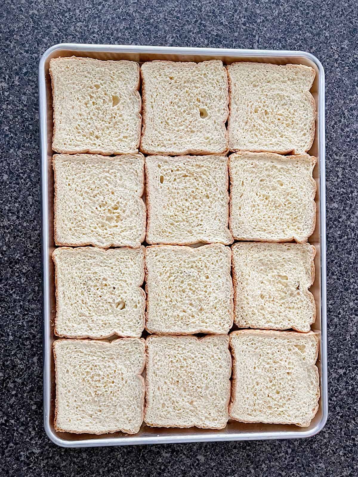 Slices of bread covered in French Toast custard on a baking sheet.