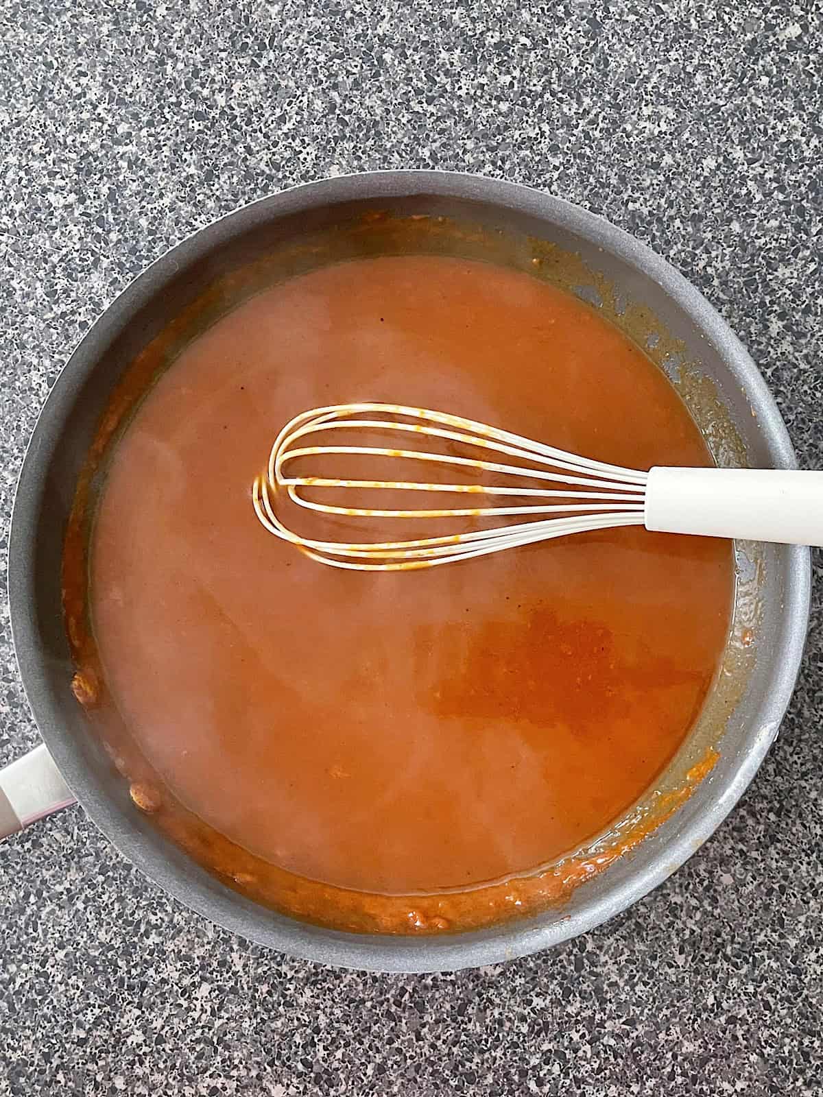 Homemade enchilada sauce in a pan with a whisk.
