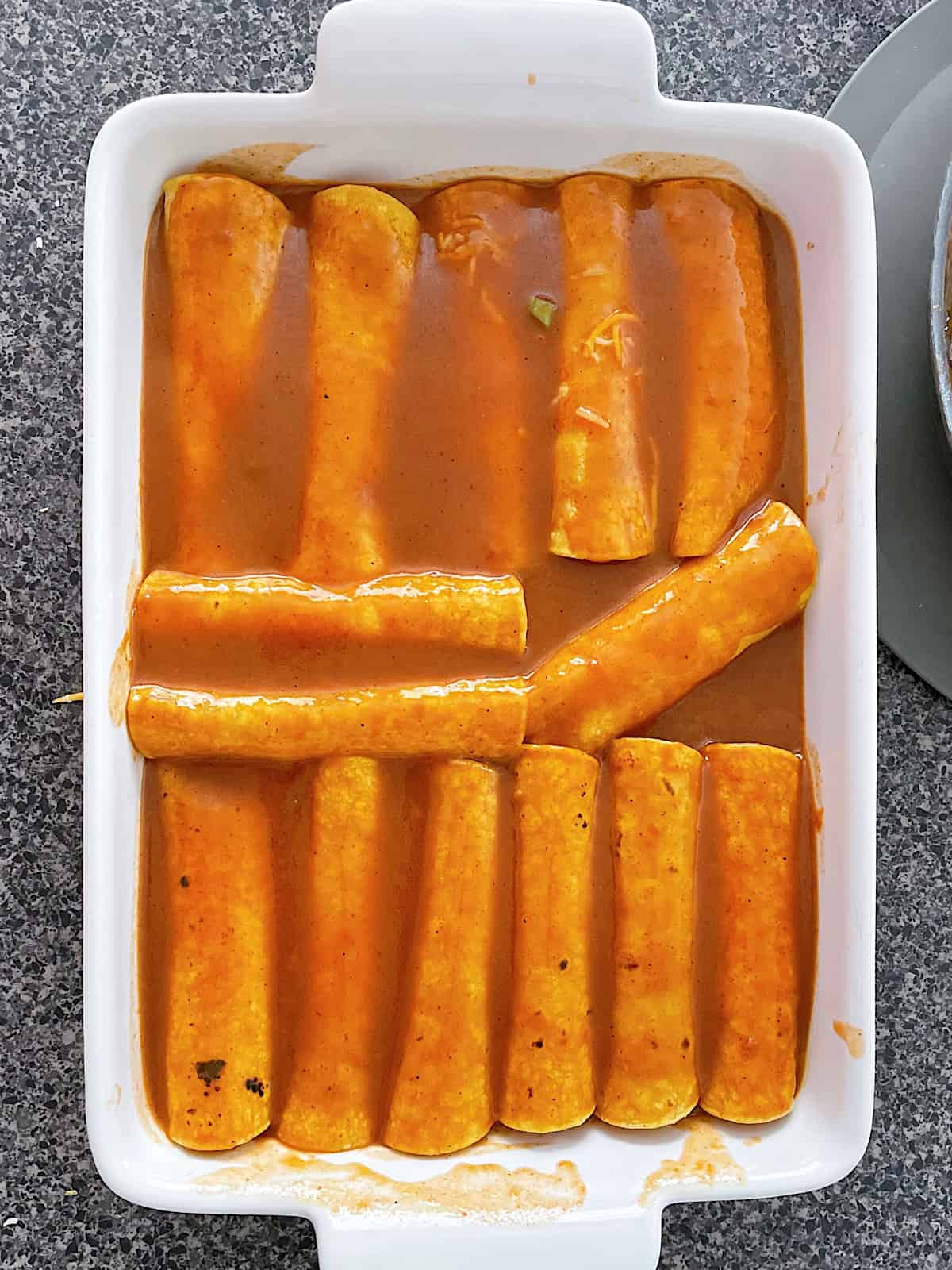 Cheese enchiladas covered in sauce in a white dish.
