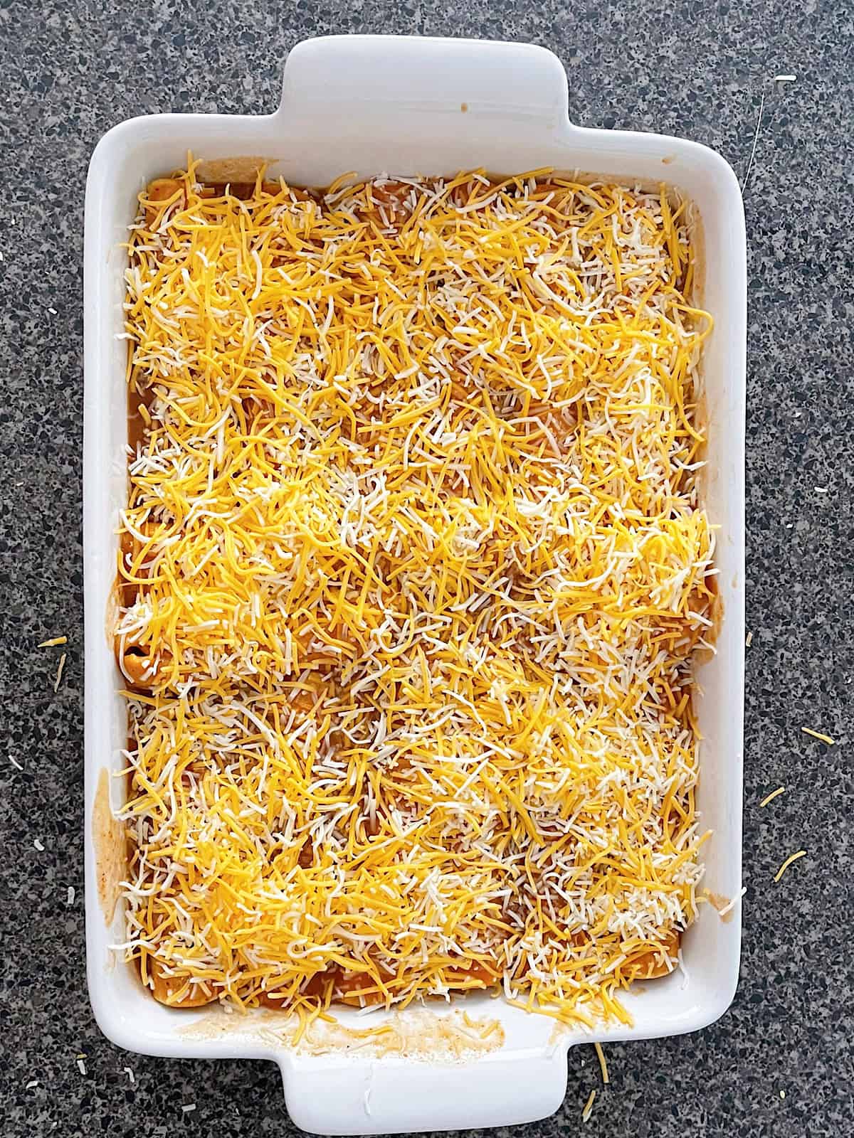 Unbaked cheese enchiladas in a white baking dish.