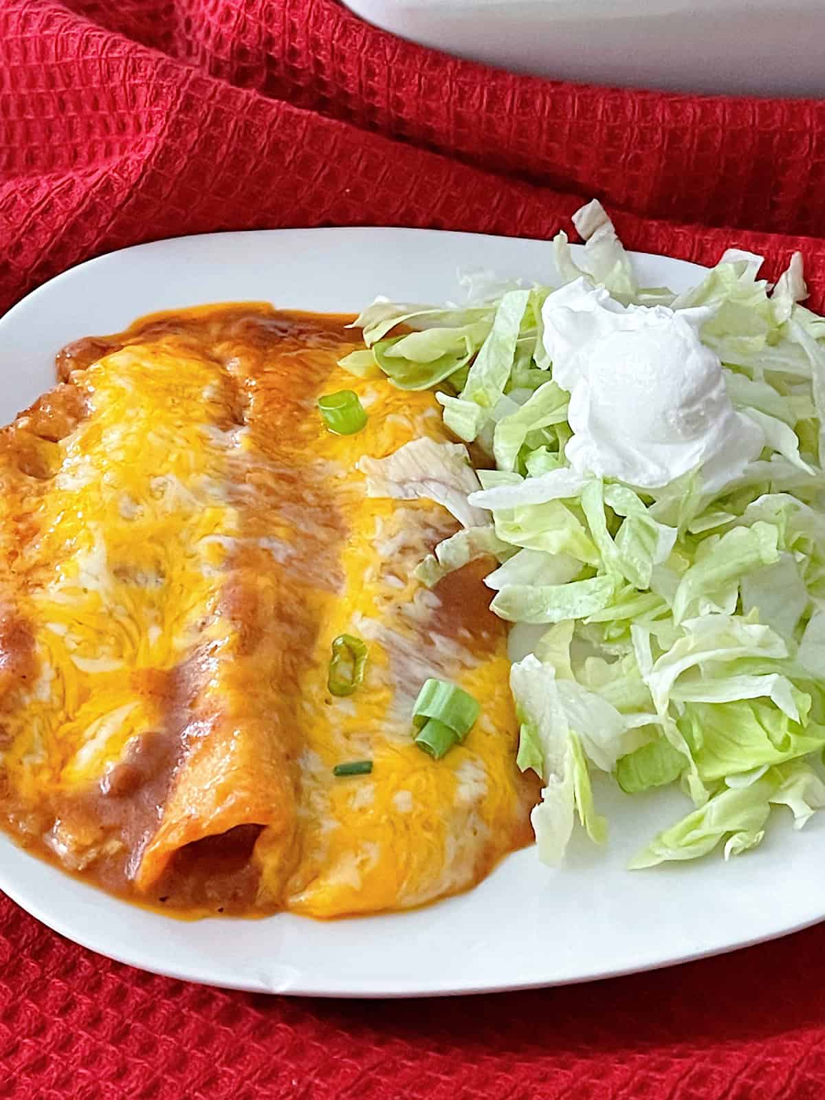 A plate of cheese enchiladas with shredded lettuce and sour cream.