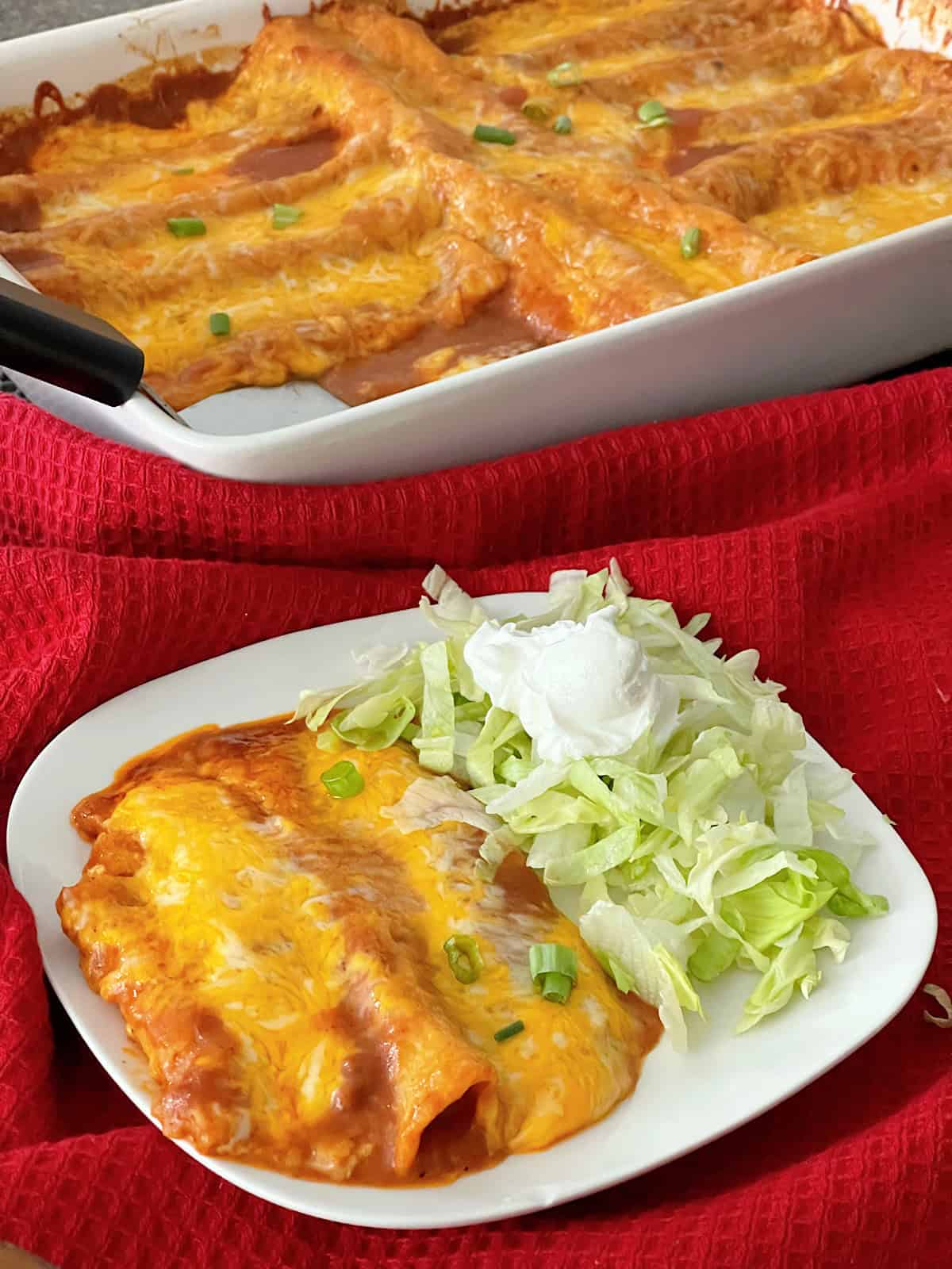 A plate of cheese enchiladas with shredded lettuce and sour cream.