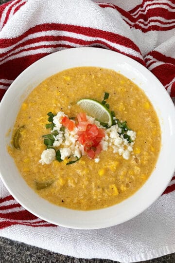 A bowl of Mexican Street Corn Soup topped with pic de gallo, cojita cheese, cilantro, and lime.