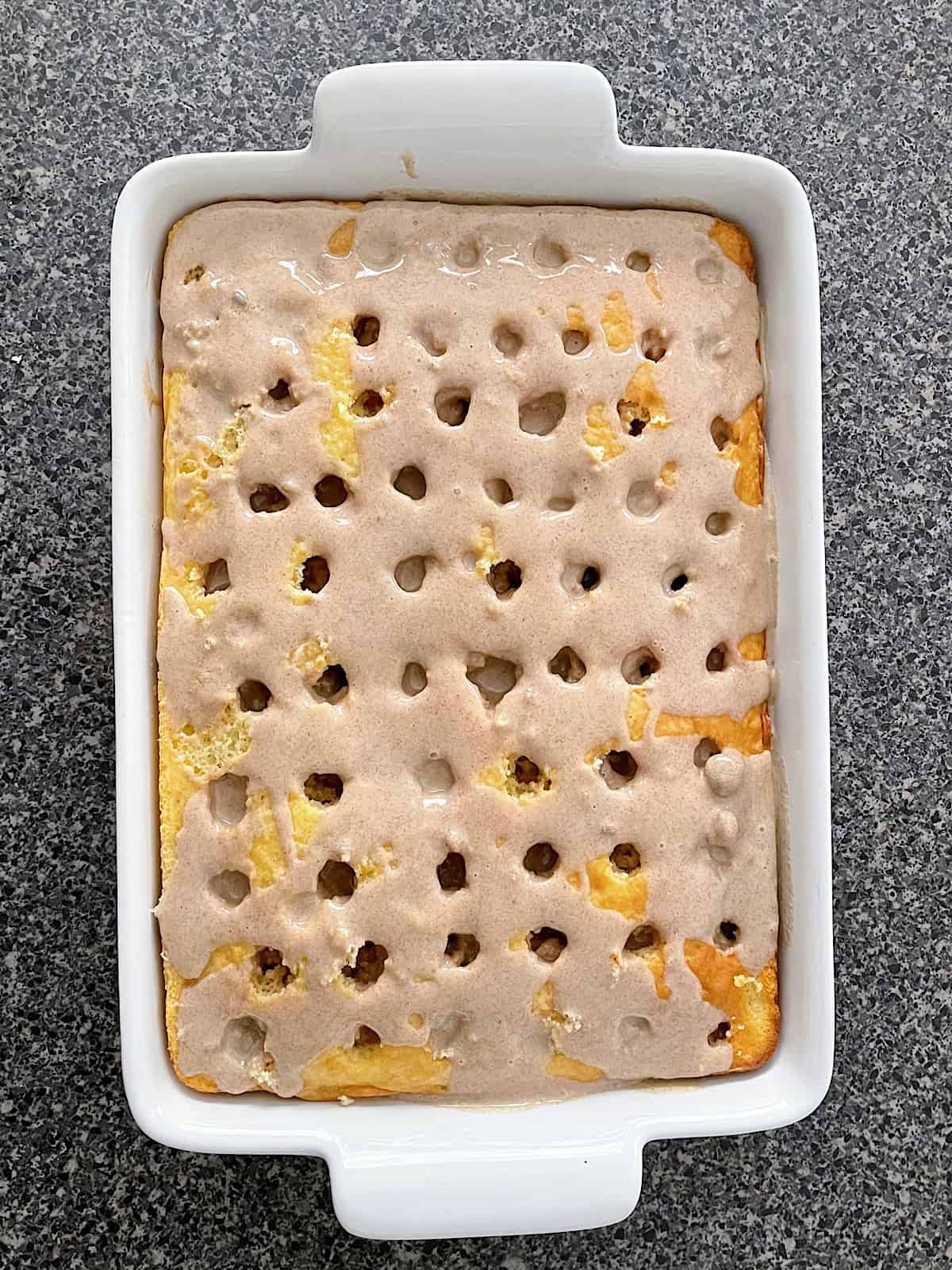 A vanilla cake with holes covered in cinnamon roll filling and sweetened condensed milk.